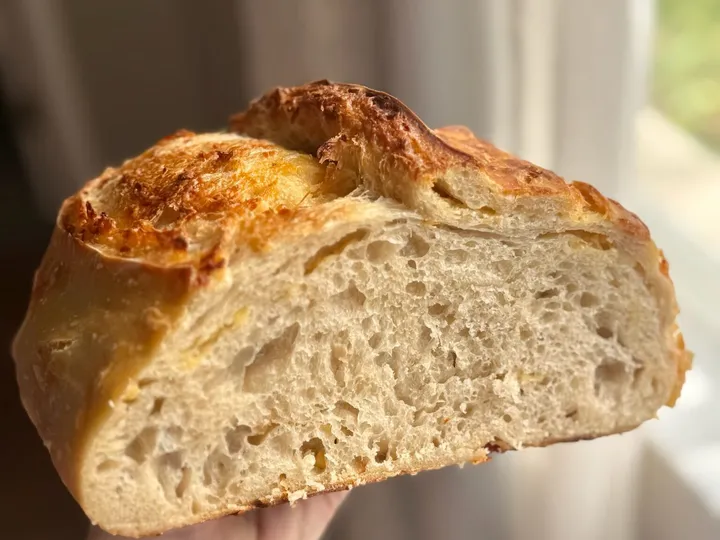 Cut sourdough loaf held by hand near a window, showing an airy interior crumb and browned crust
