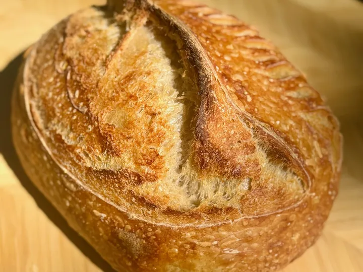 Round sourdough loaf baked with melted cheddar, photographed on a wooden board
