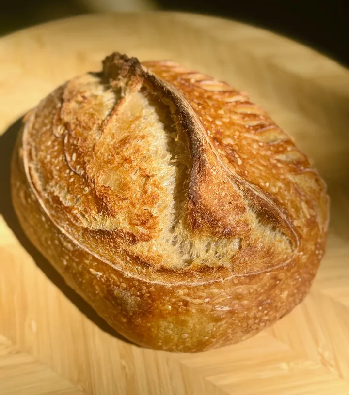 Round sourdough loaf baked with melted cheddar, photographed on a wooden board