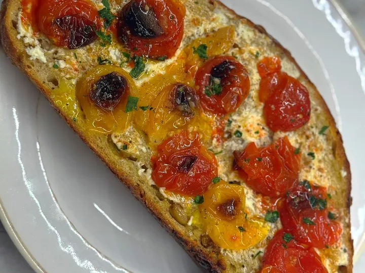 Slice of toasted sourdough topped with ricotta and blistered cherry tomatoes on a white plate