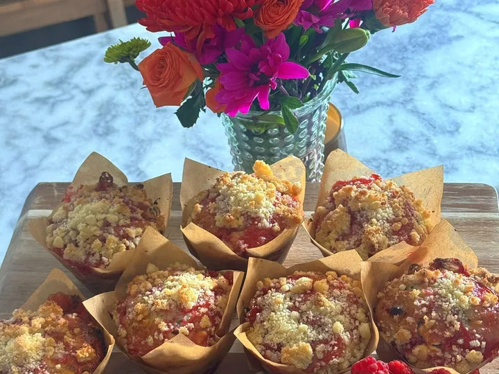 Raspberry white chocolate streusel muffins on a wooden board with raspberries and white chocolate