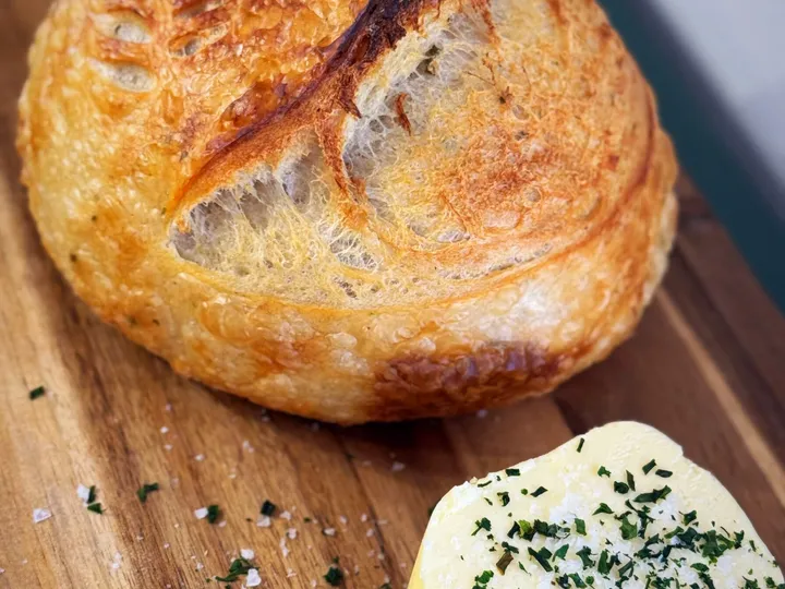 Round sourdough loaf on a wooden board beside a pat of herb butter