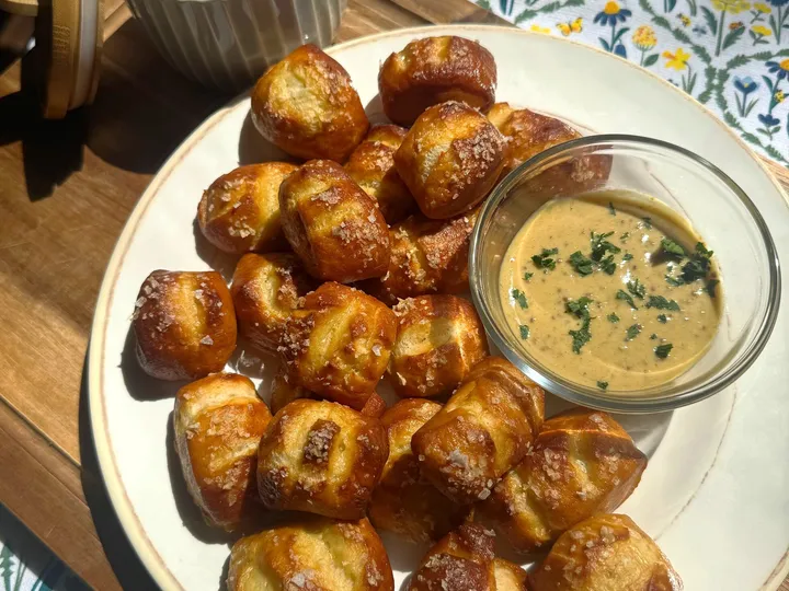 Plate of salted pretzel bites with dipping sauce and a ramekin of coarse salt on a wooden board