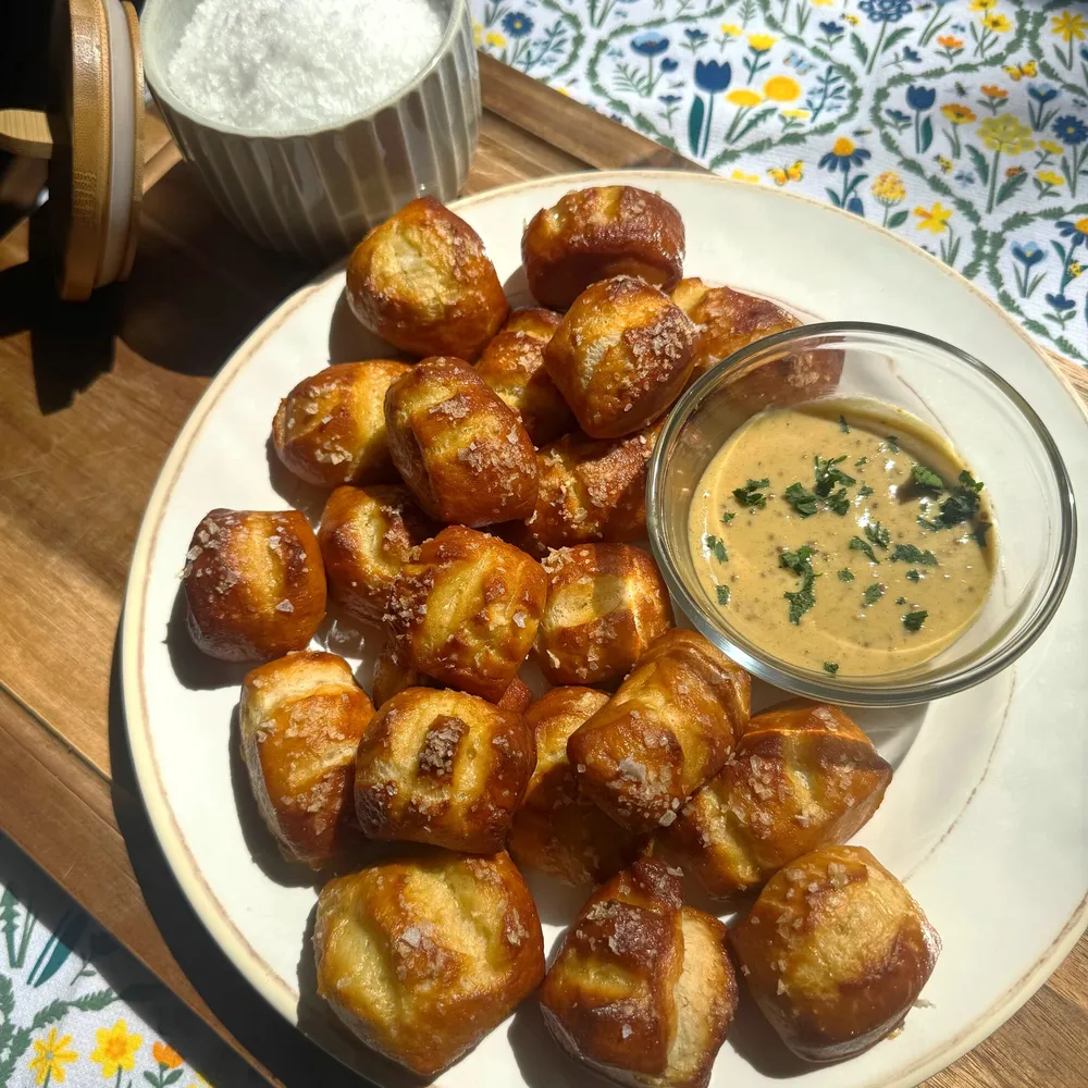 Plate of salted pretzel bites with dipping sauce and a ramekin of coarse salt on a wooden board