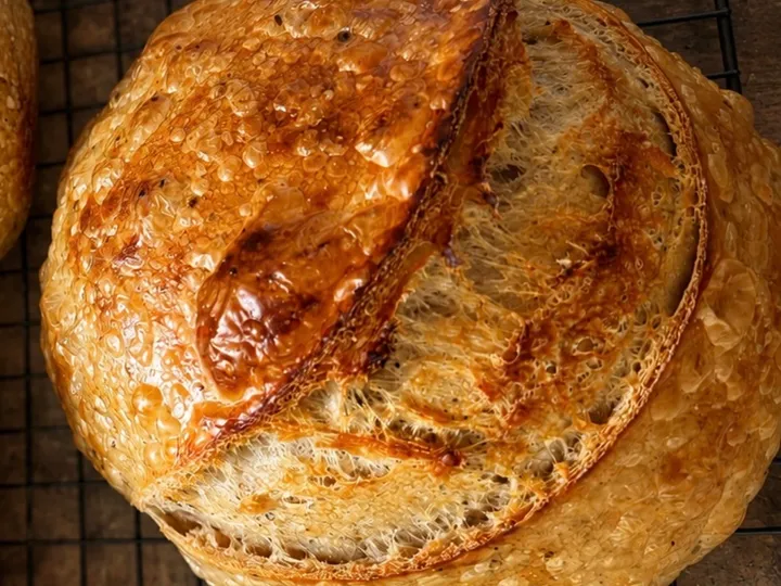 Round sourdough loaf with a deeply scored golden crust cooling on a black wire rack