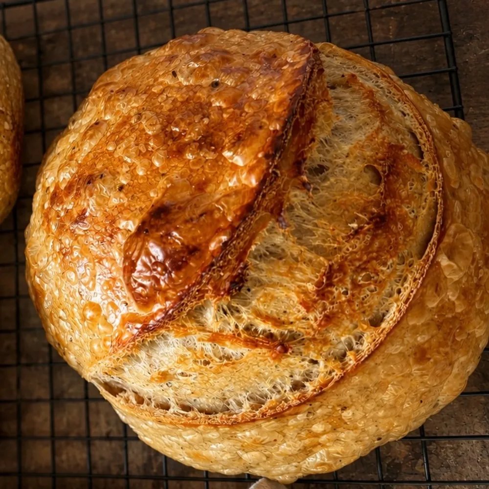 Round sourdough loaf with a deeply scored golden crust cooling on a black wire rack