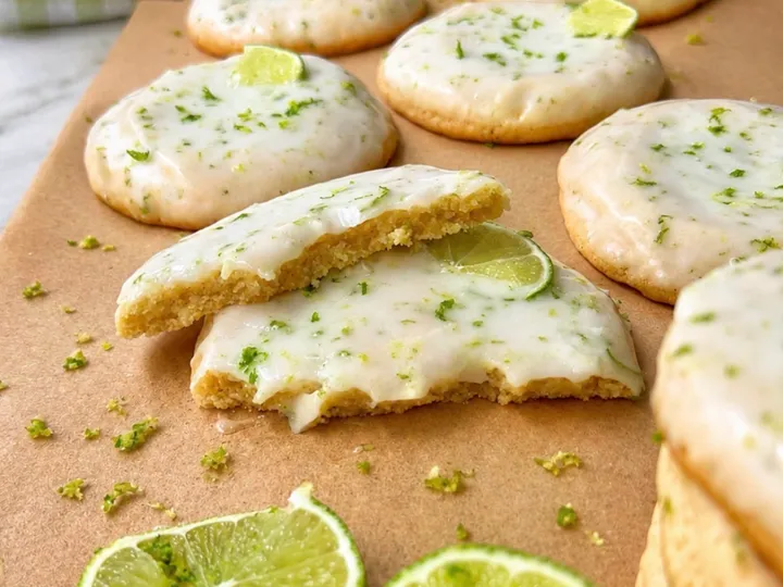 Key lime cookies with white glaze, lime zest, and lime slices on parchment paper