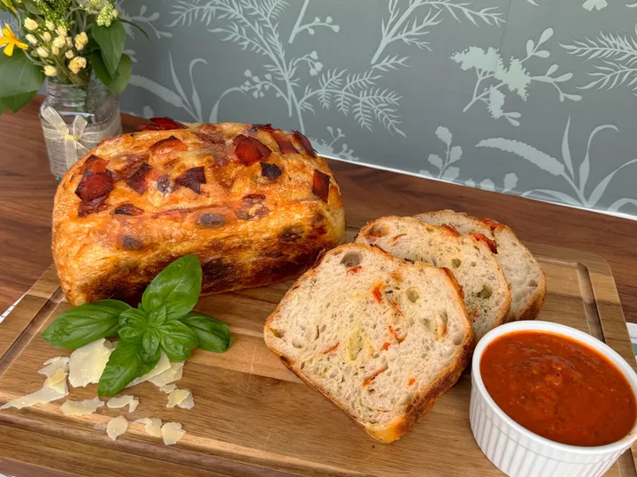 Pizza sourdough loaf with sliced bread, basil, Parmesan, and tomato sauce on a wooden board