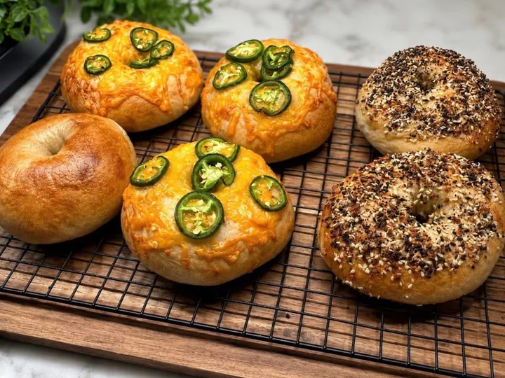 Assorted sourdough bagels with plain, everything, and jalapeno cheese flavors on a cooling rack