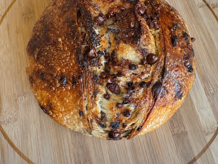 Round chocolate chip croissant sourdough loaf with a glossy crust on a wooden board