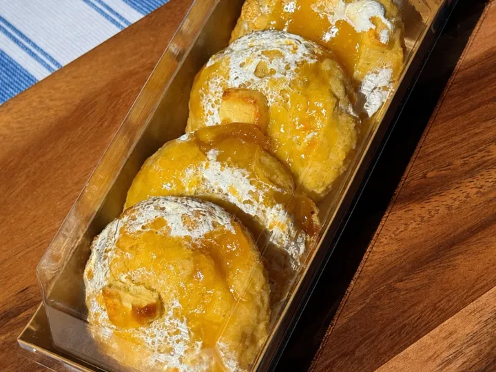 Four lemon meringue pie cookies with glossy lemon topping in a clear bakery box