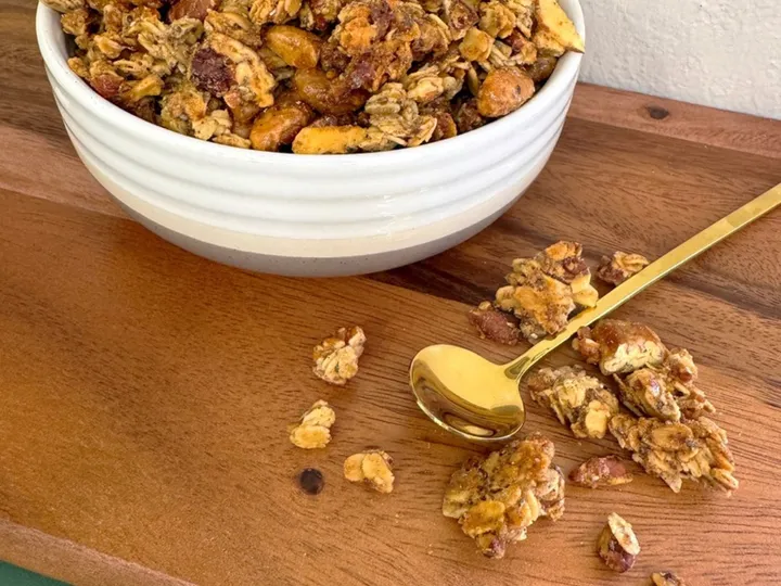 Bowl of sourdough maple pecan granola with oat clusters and nuts on a wooden board