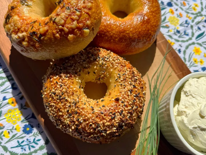 Three sourdough bagels on a wooden board with cream cheese and chives