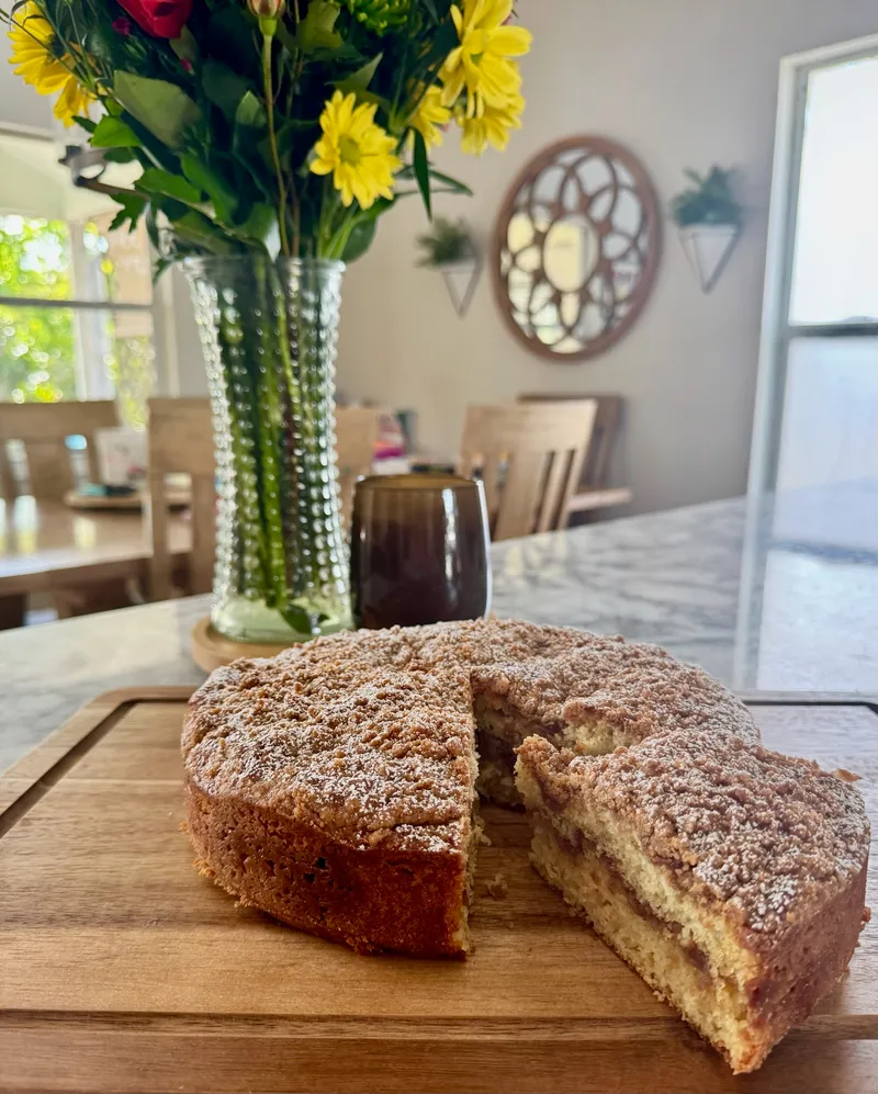 Sourdough coffee cake with crumb topping, sliced, with fresh flowers in the background