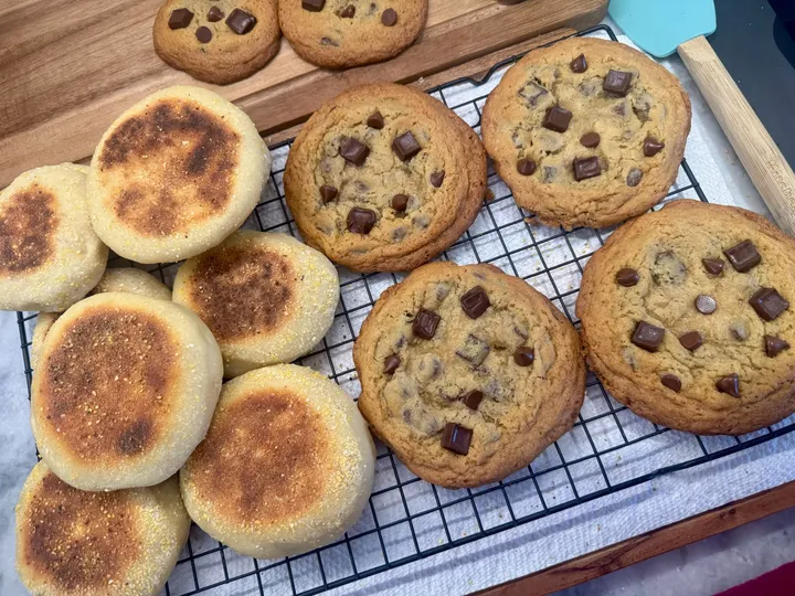 Fresh English muffins and chocolate chip cookies cooling on a wire rack